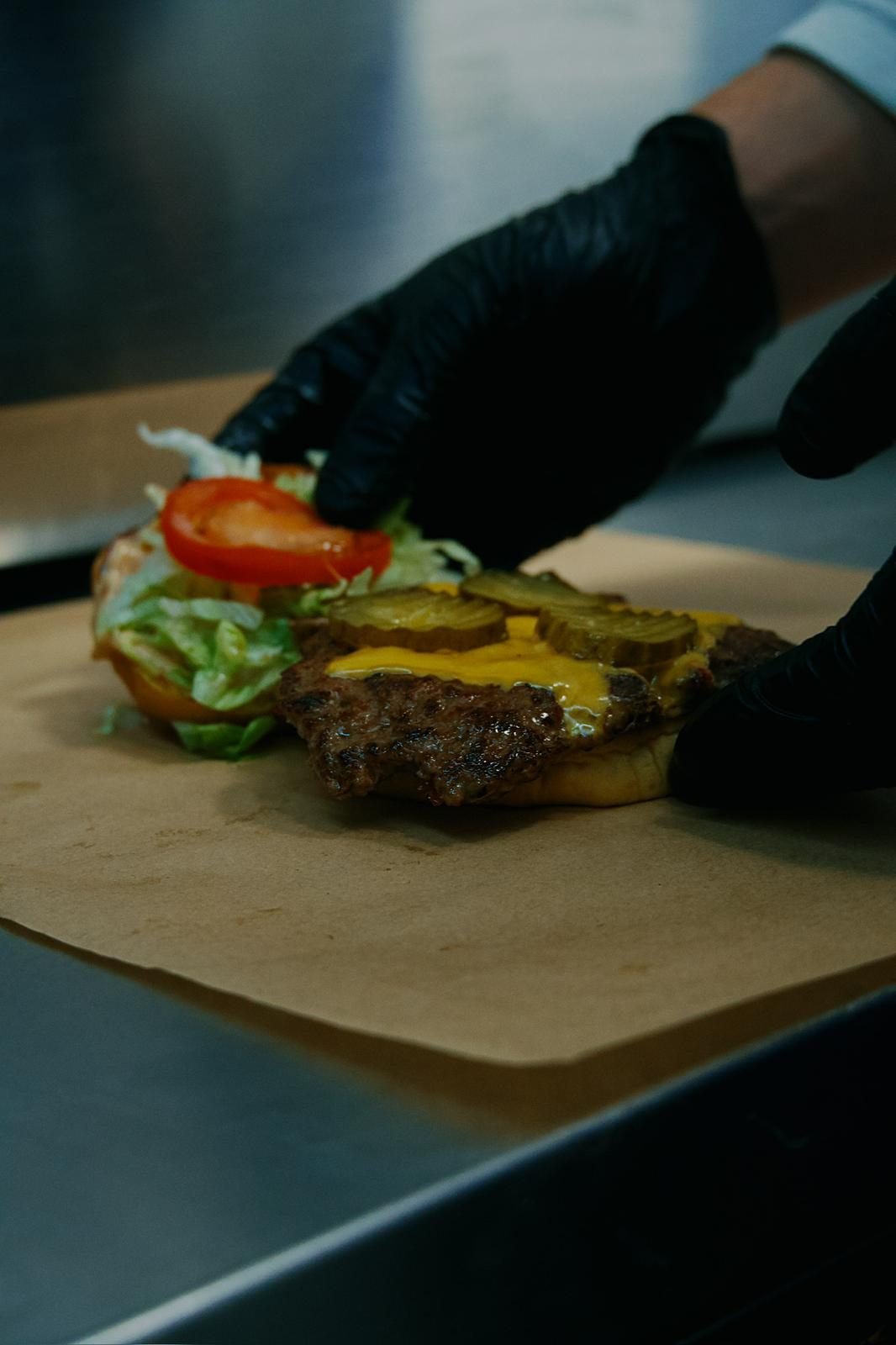 Frisches Patty wird mit Salat, Tomate und Essiggurke belegt